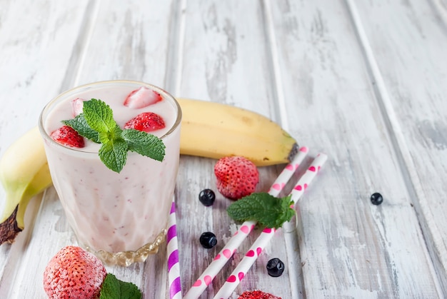 Berry smoothies of strawberries, banana  in glasses and ingredients on a wooden table