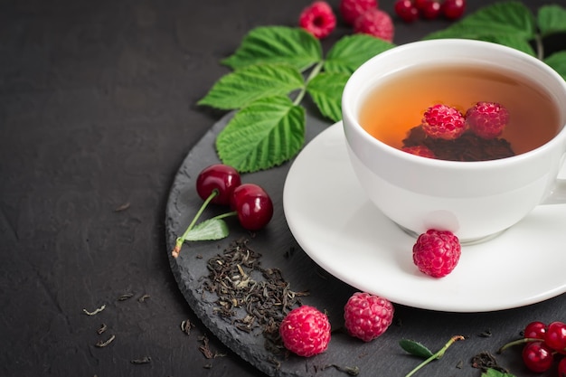 Berry tea and ripe raspberry cherry currant on a black background