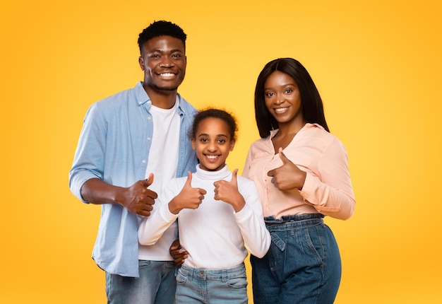 Best choice Portrait of happy black family showing thumbs up recommending something good yellow background