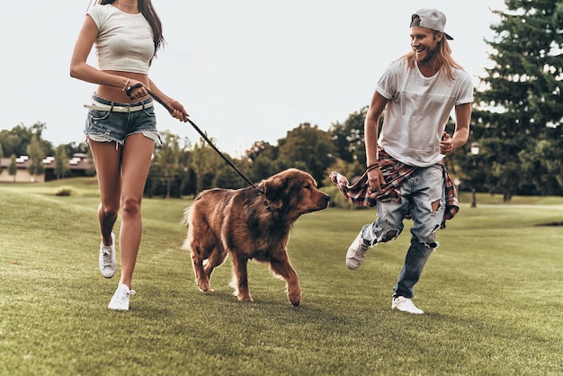 Best day ever! Young modern couple playing with their dog while running in the park