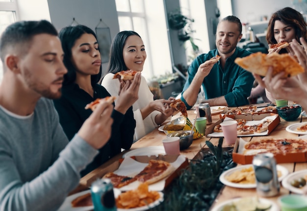 Best friends. Group of young people in casual wear eating pizza and smiling while having a dinner party indoors