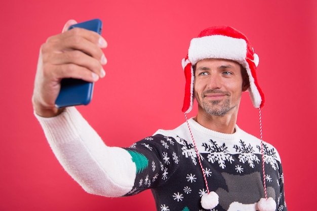 Best phone for party selfie. Santa man make video call on mobile phone. Bearded man use phone camera for holiday streaming. Stay mobile on holiday season. Happy new year. Christmas phone message.