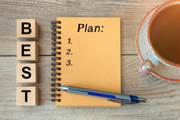 Best Plan - inscription on a notebook and wooden cubes, a cup with coffee.