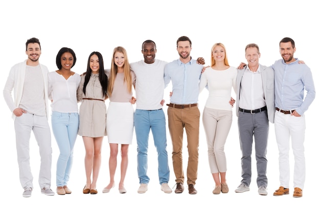 The best team ever. Full length of happy diverse group of people bonding to each other and smiling while standing against white background together