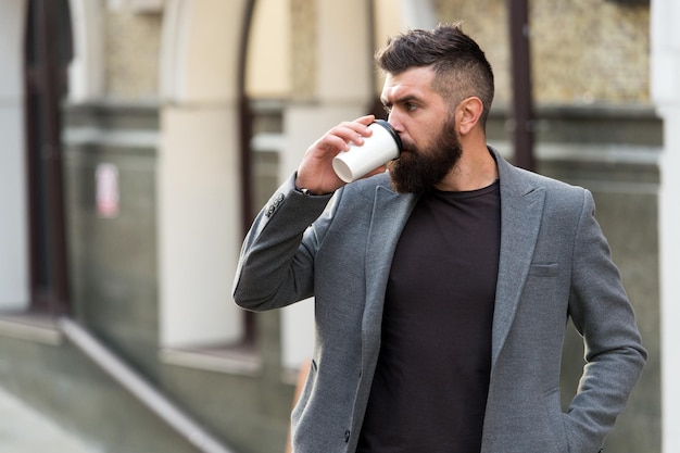 The best time to drink coffee Bearded man drinking morning coffee Businessman in hipster style holding takeaway coffee Hipster with disposable paper cup walking in city Day begins with coffee