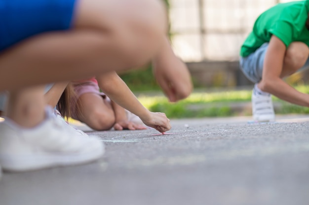 Best time. Involved interested children drawing with crayons on asphalt in park on summer day, no face