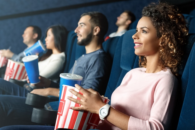 Best way to spend your day off work. Horizontal portrait of a beautiful African woman smiling cheerfully enjoying movies at the local movie theater