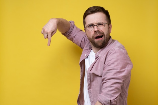 Bewildered man persistently points finger down and looks inquiringly at the camera