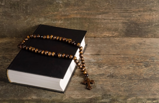 Bible with rosary on old wooden background with copy space, religion concept