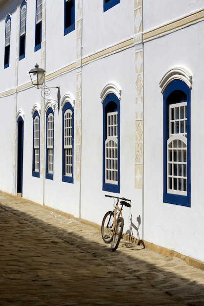 Bicycle parked next to the white wall with blue windows