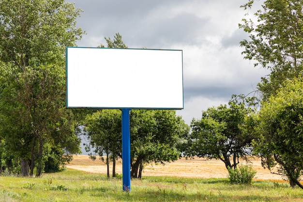 Big blank billboard mock-up along highway against meadow with trees