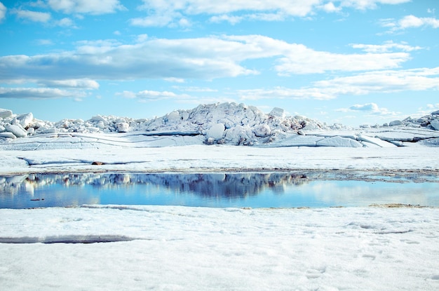 Big blocks of white ice and a puddle mirroring it on the shore of the bay on a cold clear sunny day