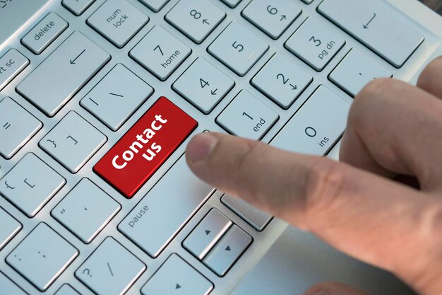 Photo big blue contact us keyboard button, red button. inscriptions on the grey silver keyboard button a male finger presses a color button on a gray silver keyboard of a modern laptop. close up.