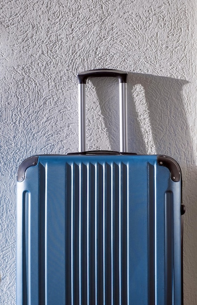 Big blue suitcase stays in the room in hotel near wall with sunlight and shadow