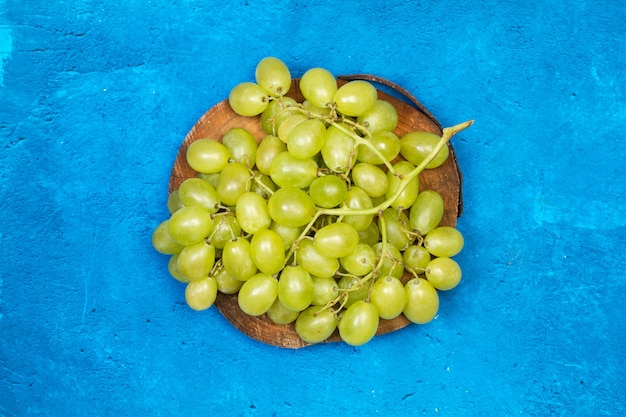 A big bunch of green grapes on a tree trunk and on a blue background