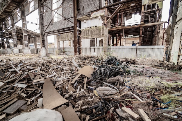 Big bunch of old rubbish on the background of a ruined plant. Pile of wooden pieces lays on a dirty floor. Environment pollution concept