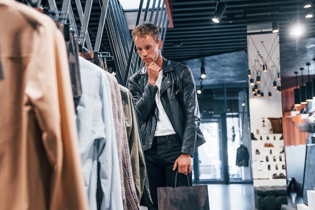 Big choice Young guy in modern store with new clothes Elegant expensive wear for men