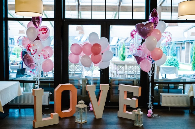 Big decorated letters Love and inflatable pink and white balls with helium are on a wooden floor in a restaurant in the area for the wedding ceremony Photo Zone on day of lovers and valentines day