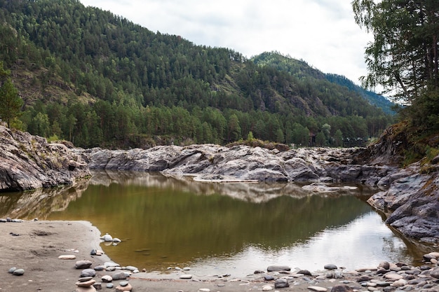 A Big fast-flowing wide and full-flowing mountain river. Large rocks stick out of the water.