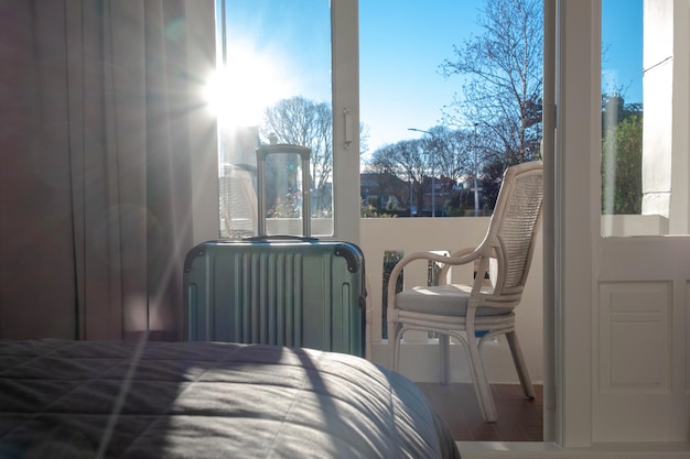 Big green suitcase stays in the room in hotel near window or balcony with sunlight