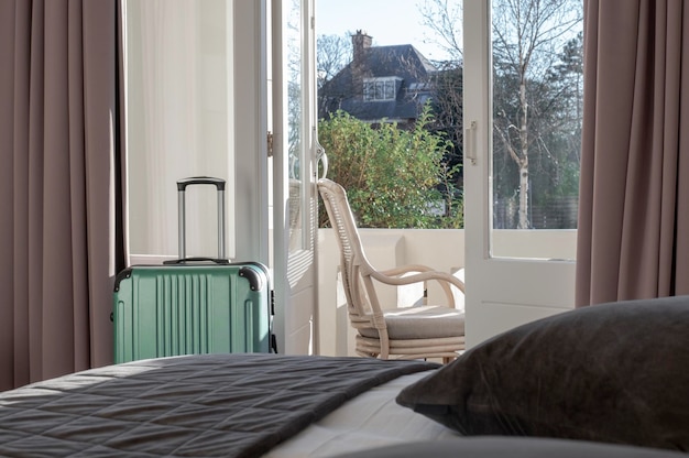 Big green suitcase stays in the room in hotel near window or balcony with sunlight