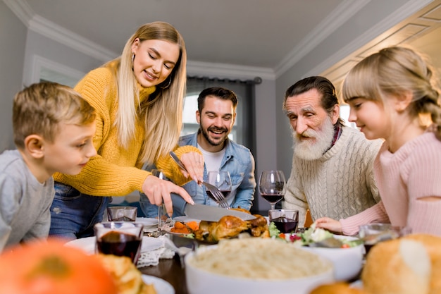 Big happy family eating Thanksgiving dinner. Roasted turkey on dining table. Parents and children having festive meal. Pretty mother cutting meat.