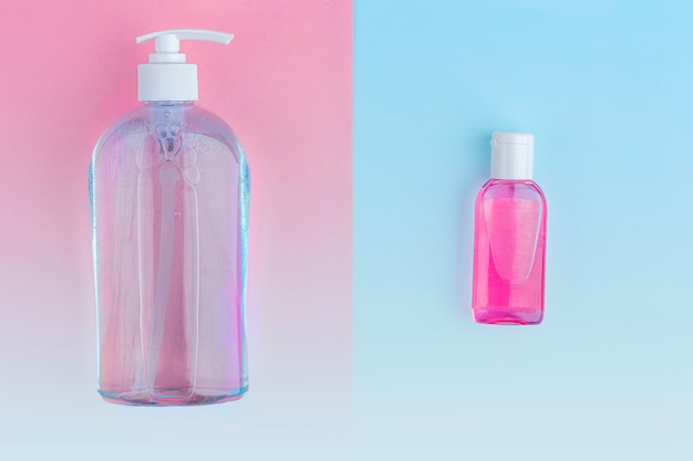 big and little bottles with antiseptic sanitizer gel for washing hands on blue and pink background. Alcohol gel as coronavirus prevention. Viral disease prevention concept.