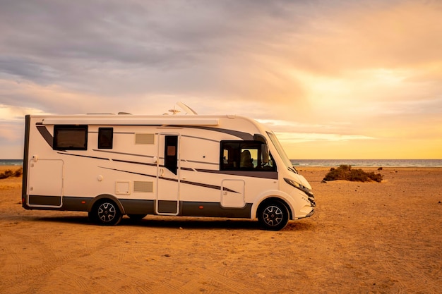 Big modern motorhome camper van parked on the ground and beautiful beach with sea and sunset lights in background. Concept of summer travel holiday vacation with camping car free