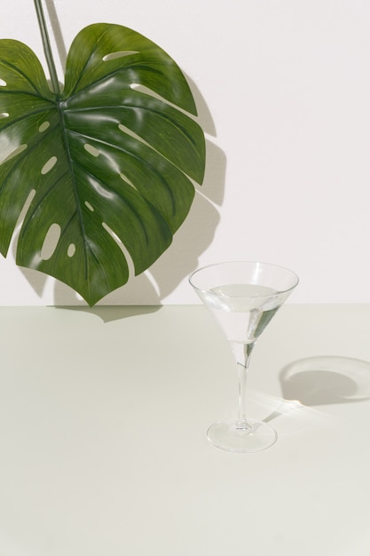 Big Monstera leaf and glass with refreshment against bright pastel background. Fancy modern minimal food and drink concept.