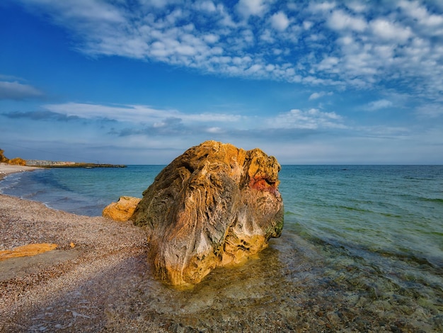 Big old stone on the seashore in sunny day blue sky and white clouds