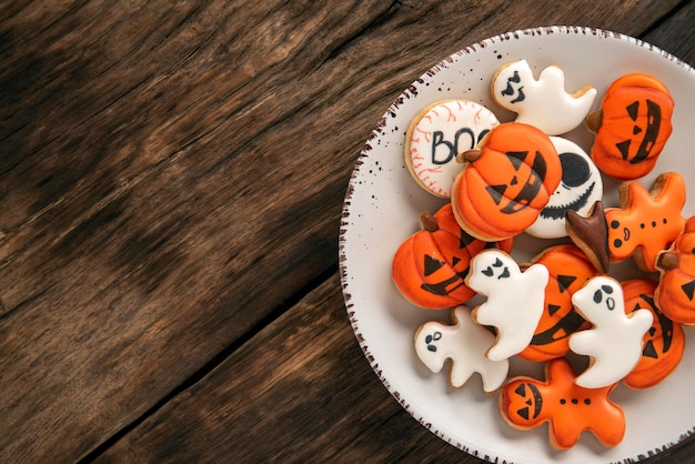 Big plate of bright orange Halloween cookies in the shape of pumpkin ghosts on a wooden table Place for text Top view