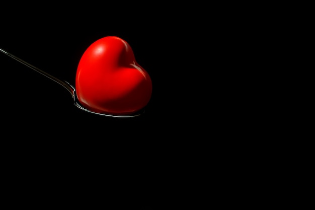 Big red heart on a metal spoon on black background