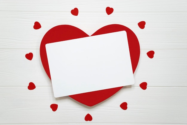 Photo big red heart with empty card and many little hearts on white textured wooden board