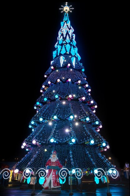 big sparkling city christmas tree at night with Santa Claus at the base