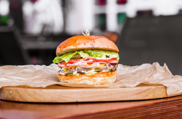 Big tasty beef burger or hamburger on wooden plate with craft paper on wooden table in outdoor street cafe Having brunch on sunny day fastfood