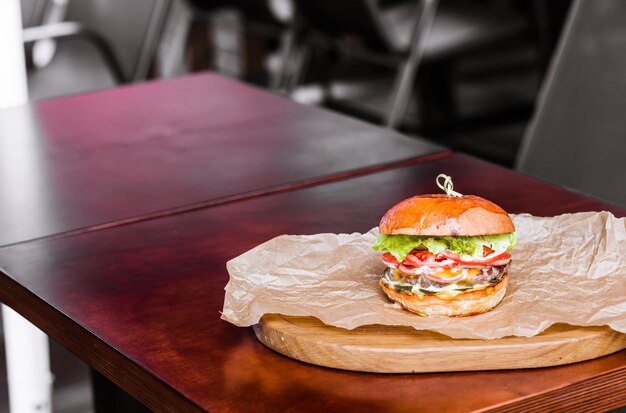 Big tasty beef burger or hamburger on wooden plate with craft paper on wooden table in outdoor street cafe Having brunch on sunny day fastfood