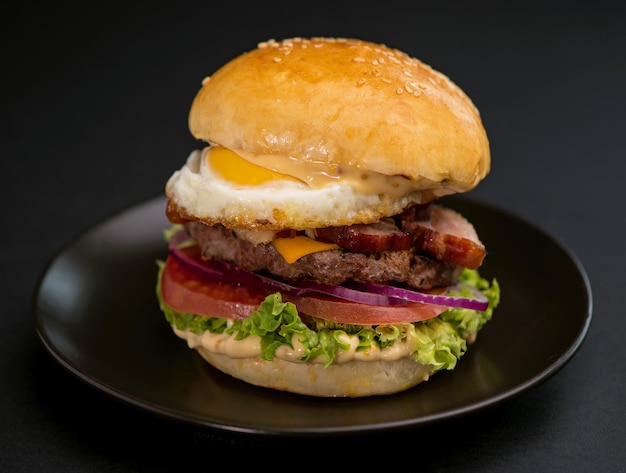 Big tasty burger with beef cutlet lettuce egg and cheese on a black background