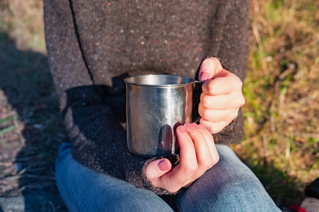 Big tourist cup in female hands. Close up shot of a woman holding a metal cup outdoors