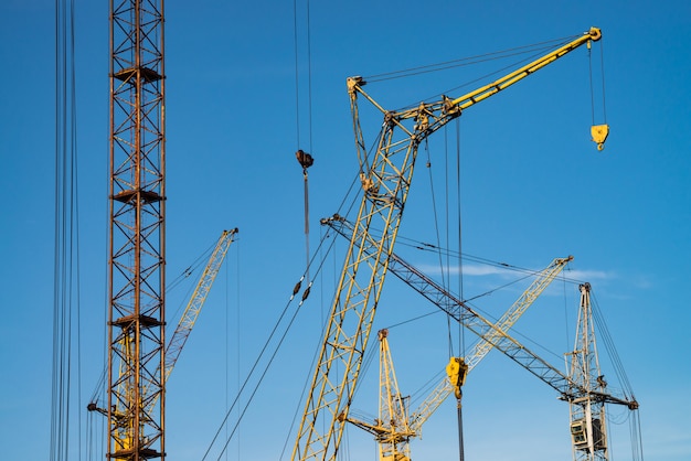 Big tower cranes against the blue sky. Background image of construction equipment close-up with copy space. Build of city.