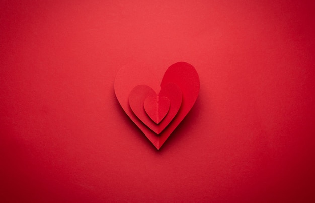 Big voluminous red heart cut from paper on red monochrome background, paper craft origami style, from above. Romantic Valentine's day symbol, love concept. Paper art design, 14 February celebration