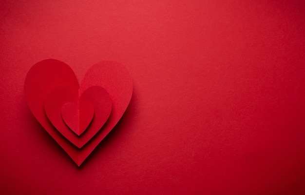 Big voluminous red heart cut from paper on red monochrome background, paper craft origami style, from above. Romantic Valentine's day symbol, love concept. Paper art design, 14 February, copy space