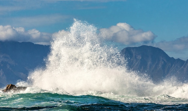 Big waves break on the rocks in the sea against the backdrop of the coastline.