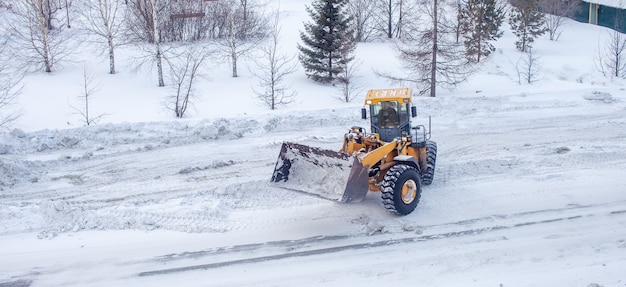 Big yellow tractor cleans up snow from the road and loads it into the truck. Cleaning and cleaning of roads in the city from snow in winter