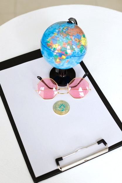 Biitcoin, glasses and a globe with space for text on a white table