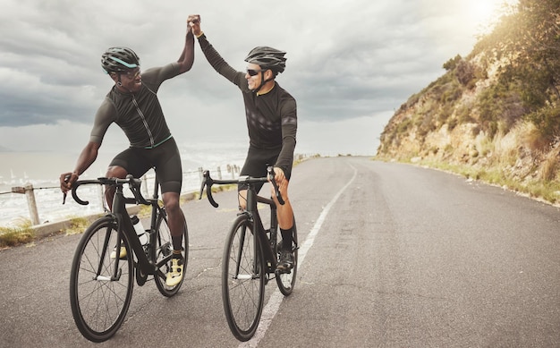 Bike friends and men high five on road having fun cycling together outdoors Success diversity and teamwork of male cyclists on bicycles riding on street exercise or workout training on asphalt