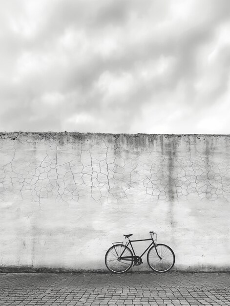 Photo a bike is parked against a wall with a cloudy sky in the background