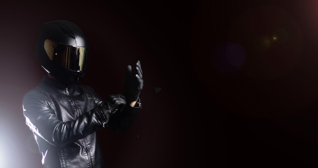 Biker motorcyclist in a protective motorcycle jacket with gloves and a helmet on a dark background.