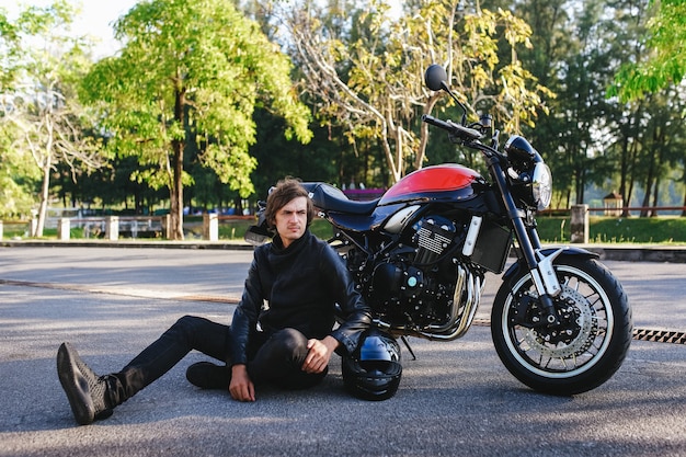 Biker sits next to his motorcycle on the road in the park