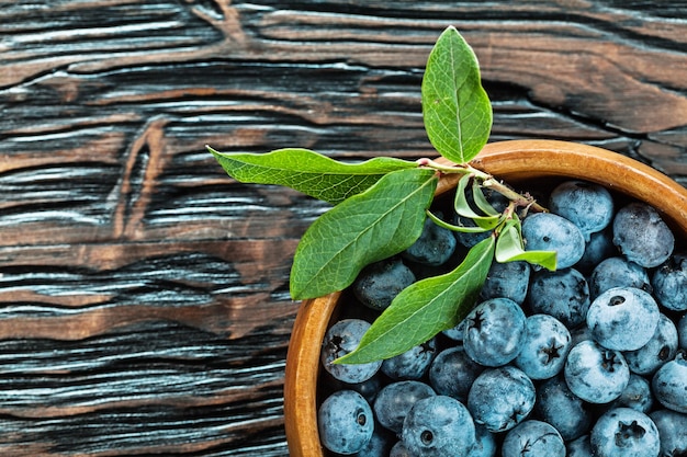 Bilberries in round wooden bowl on wood board