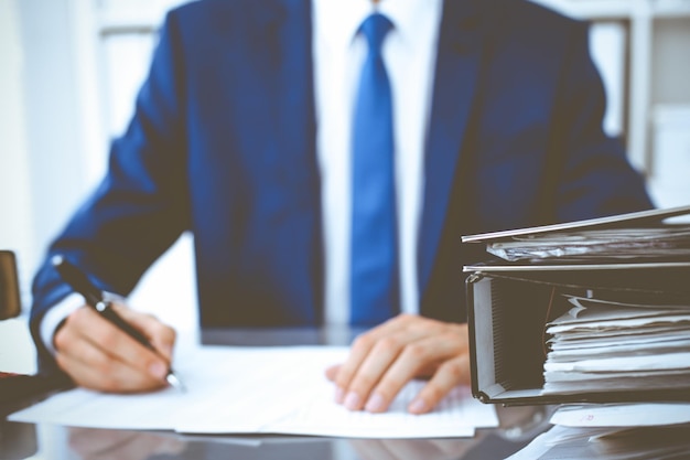 Binders with papers waiting to be processed with businessman or bookkeeper back in blur. Accounting planning budget. Audit, insurance and business concept